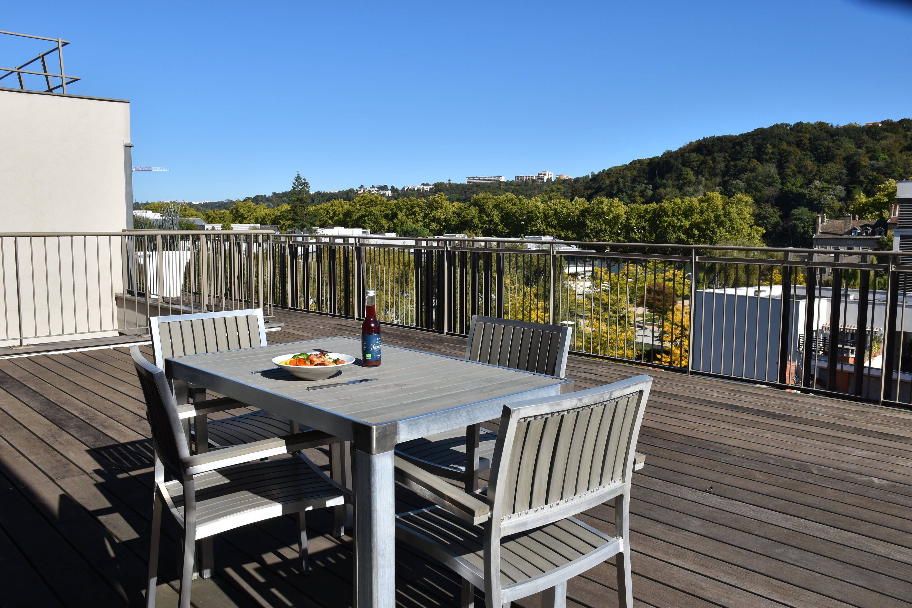 A wooden deck with a table and chairs, overlooking a forested hillside.