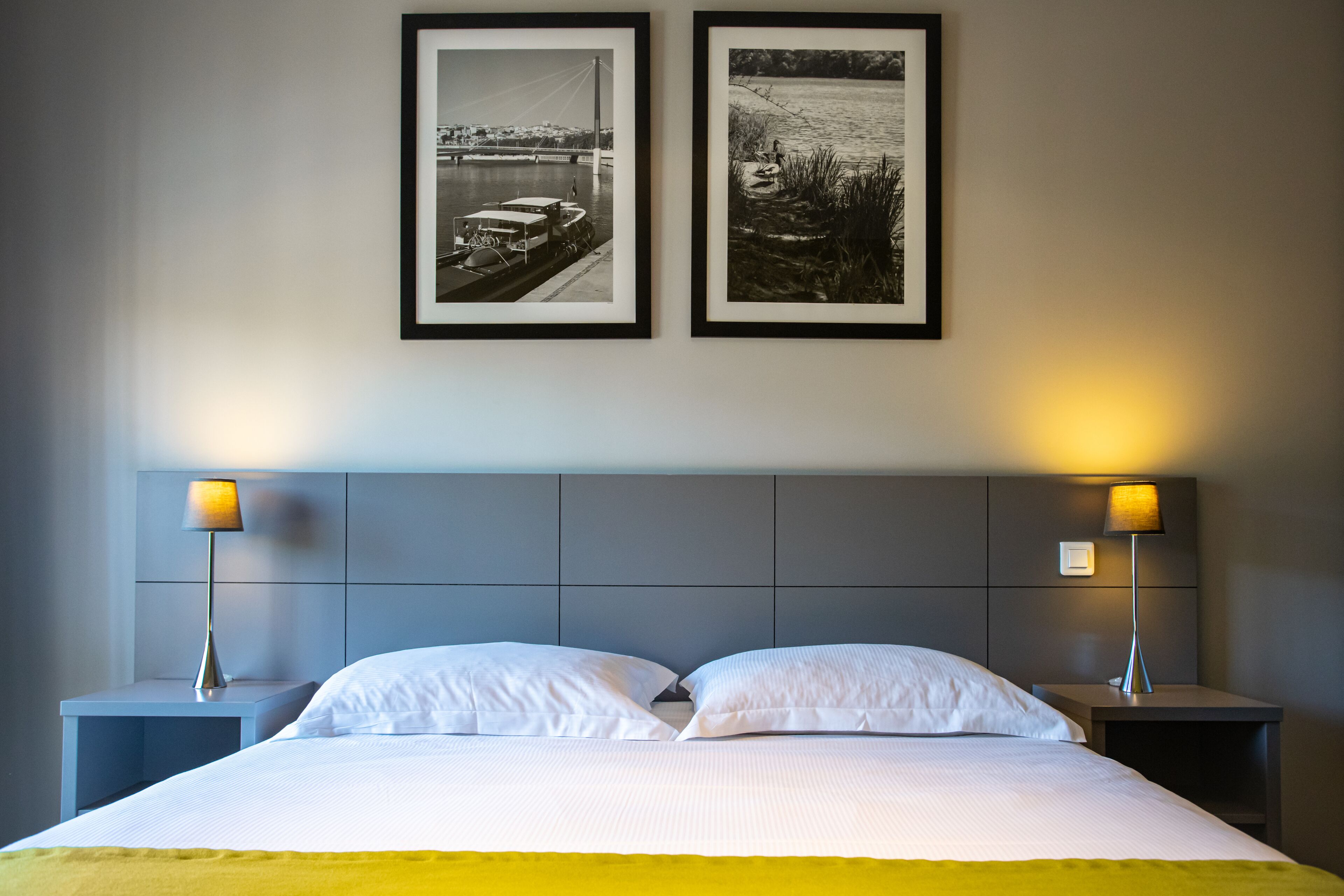 Een hotelkamer met een bed, twee nachtkastjes, twee ingelijste foto’s en twee lampen.