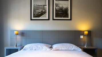 Een hotelkamer met een bed, twee nachtkastjes, twee ingelijste foto’s en twee lampen.
