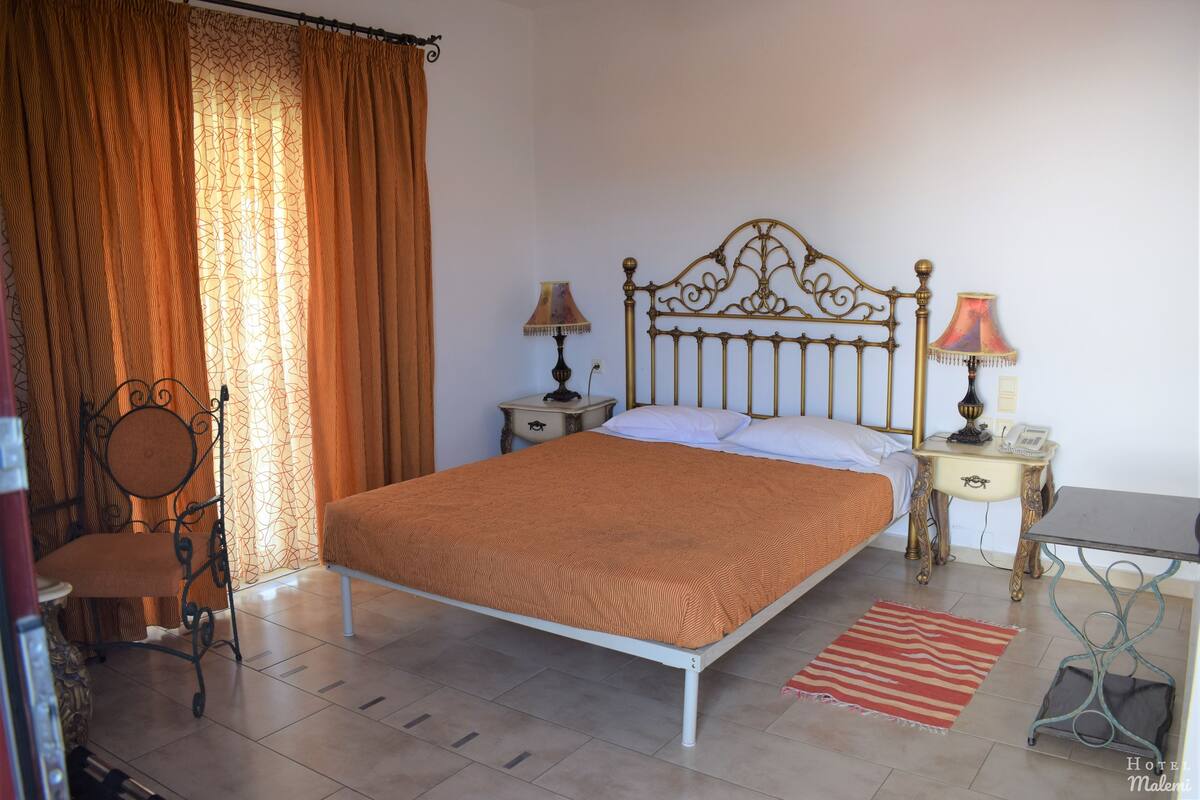 A neatly arranged bedroom with a single bed, two bedside tables, a chair, and a small table.