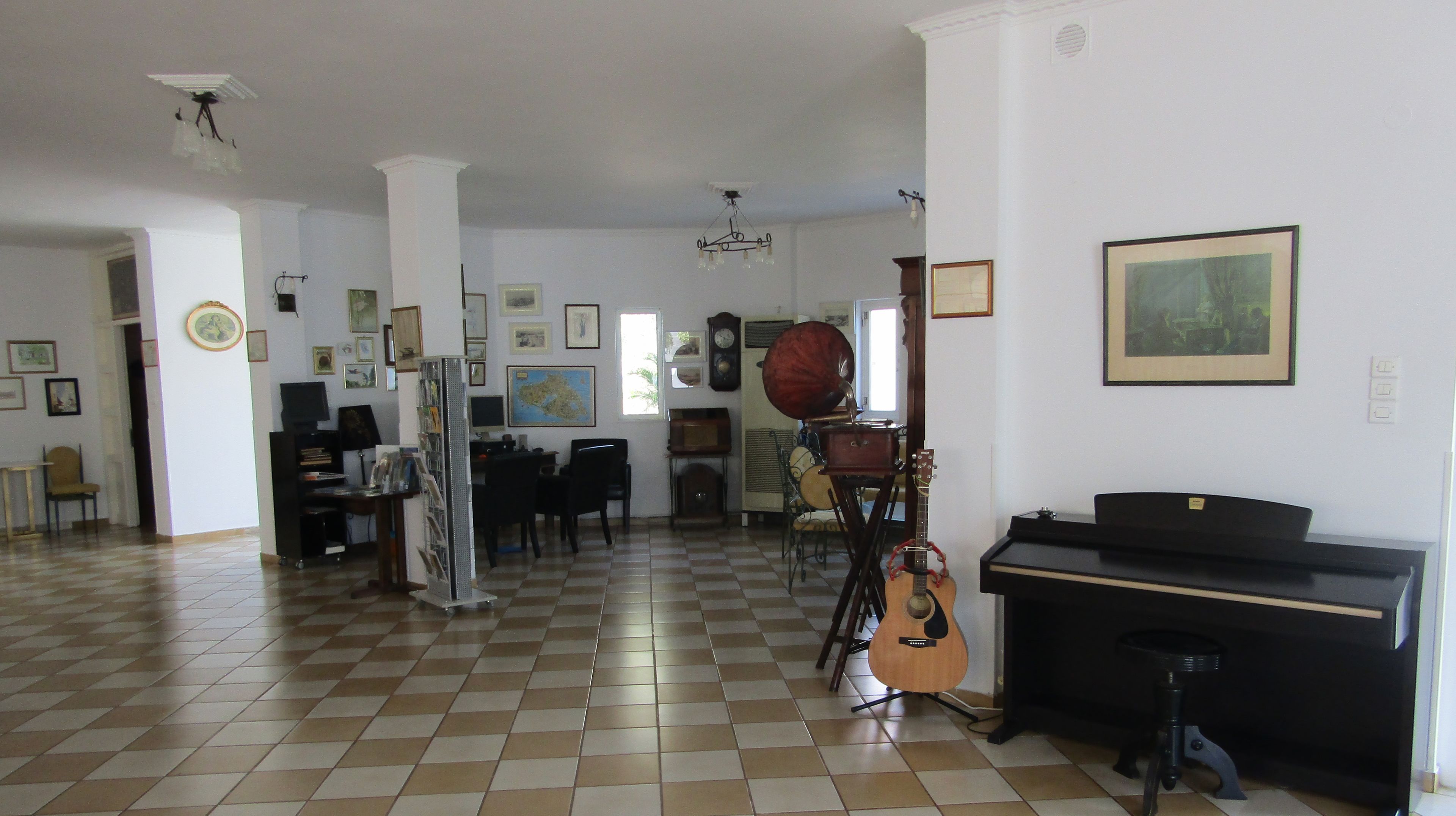 A spacious room with a checkered floor, a piano, a guitar, and various framed pictures on the walls.