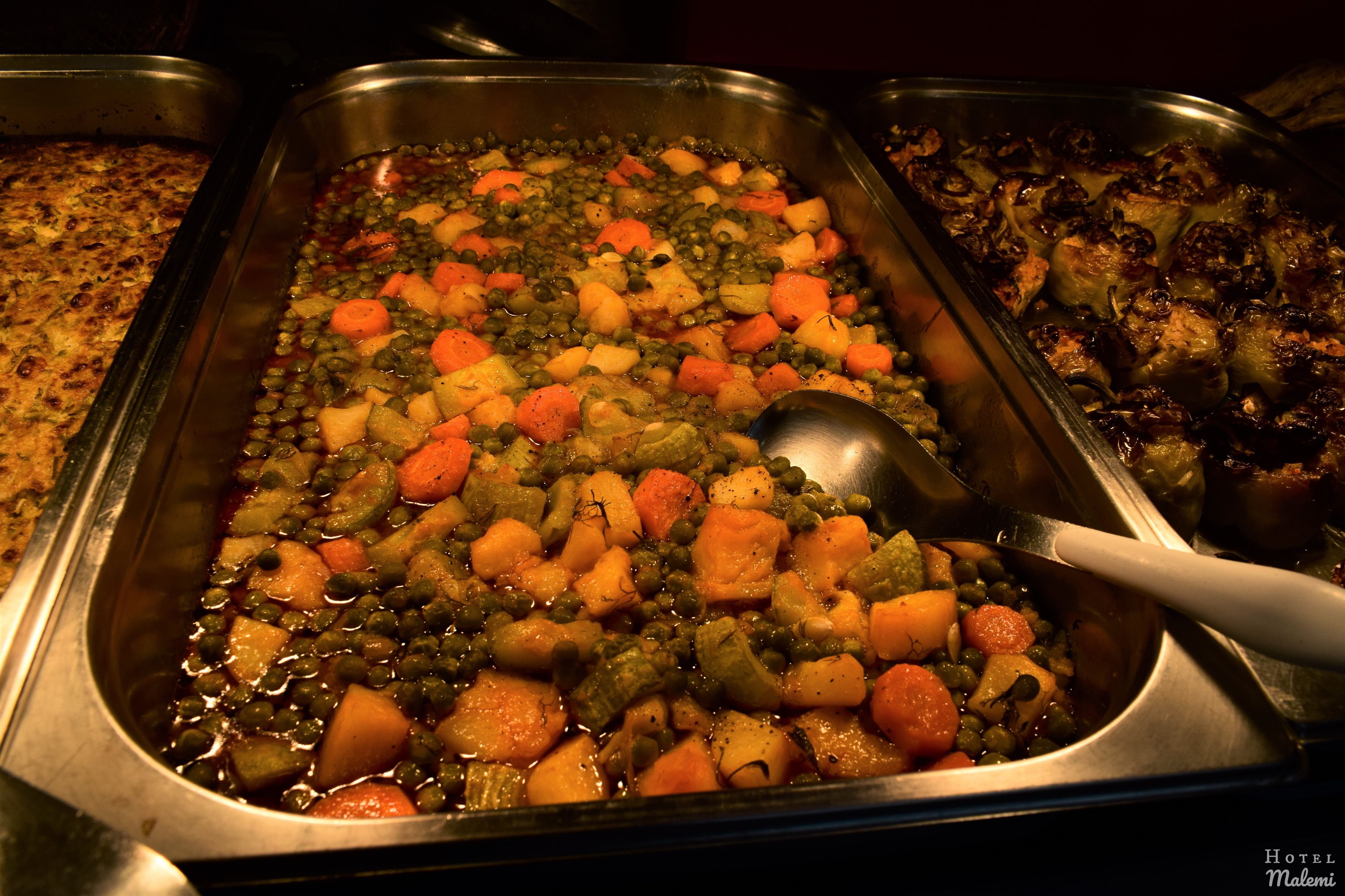 A buffet with various dishes including a vegetable casserole and roasted meats.