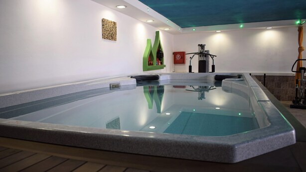 A modern indoor swimming pool with a clear water surface, surrounded by a stone wall and a wooden deck. - Malemi Organic Hotel (Lesvos)