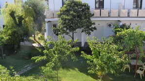 A courtyard with a lawn, trees, a wooden table, and chairs. - Malemi Organic Hotel (Lesvos)