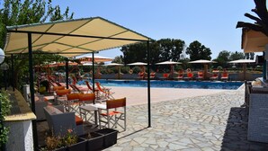 A poolside area with lounge chairs and umbrellas, a stone-tiled floor, and a clear blue sky. - Malemi Organic Hotel (Lesvos)