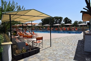 A poolside area with lounge chairs and umbrellas, a stone-tiled floor, and a clear blue sky. - Malemi Organic Hotel (Lesvos)