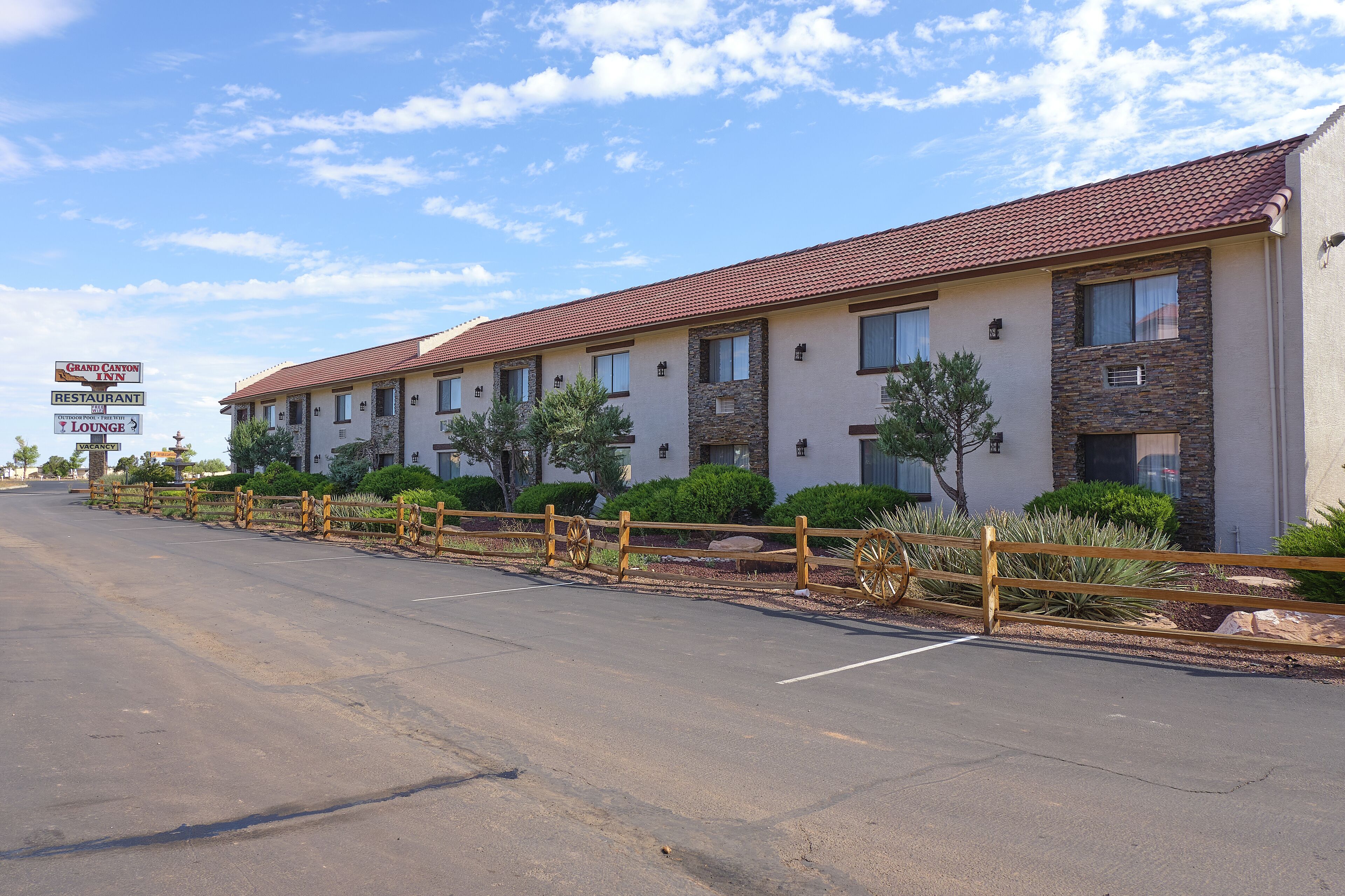 A motel with a red-tiled roof, multiple rooms, and a fenced parking area.