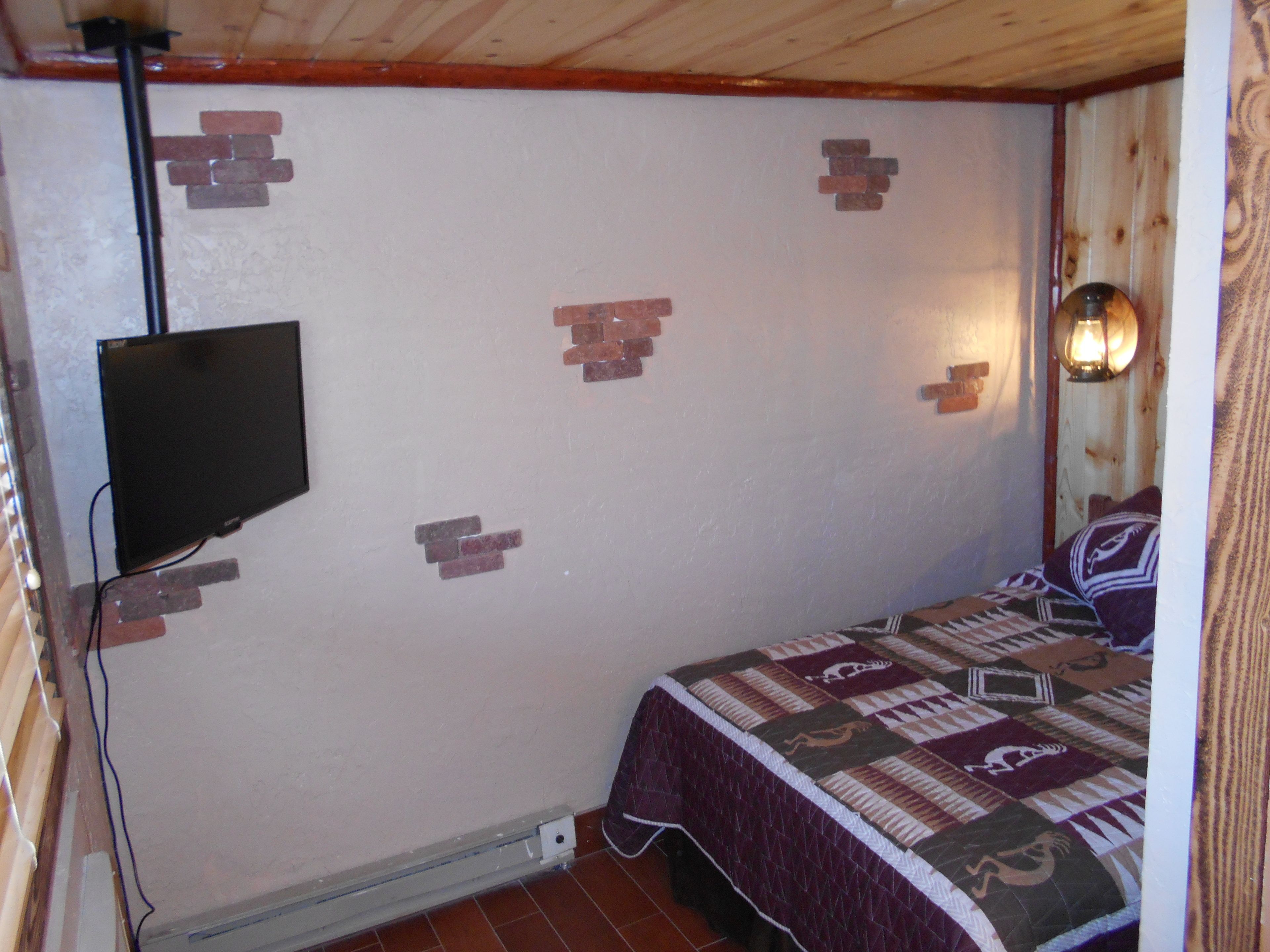 A bedroom with a bed, a wall-mounted TV, and a wall-mounted light fixture.