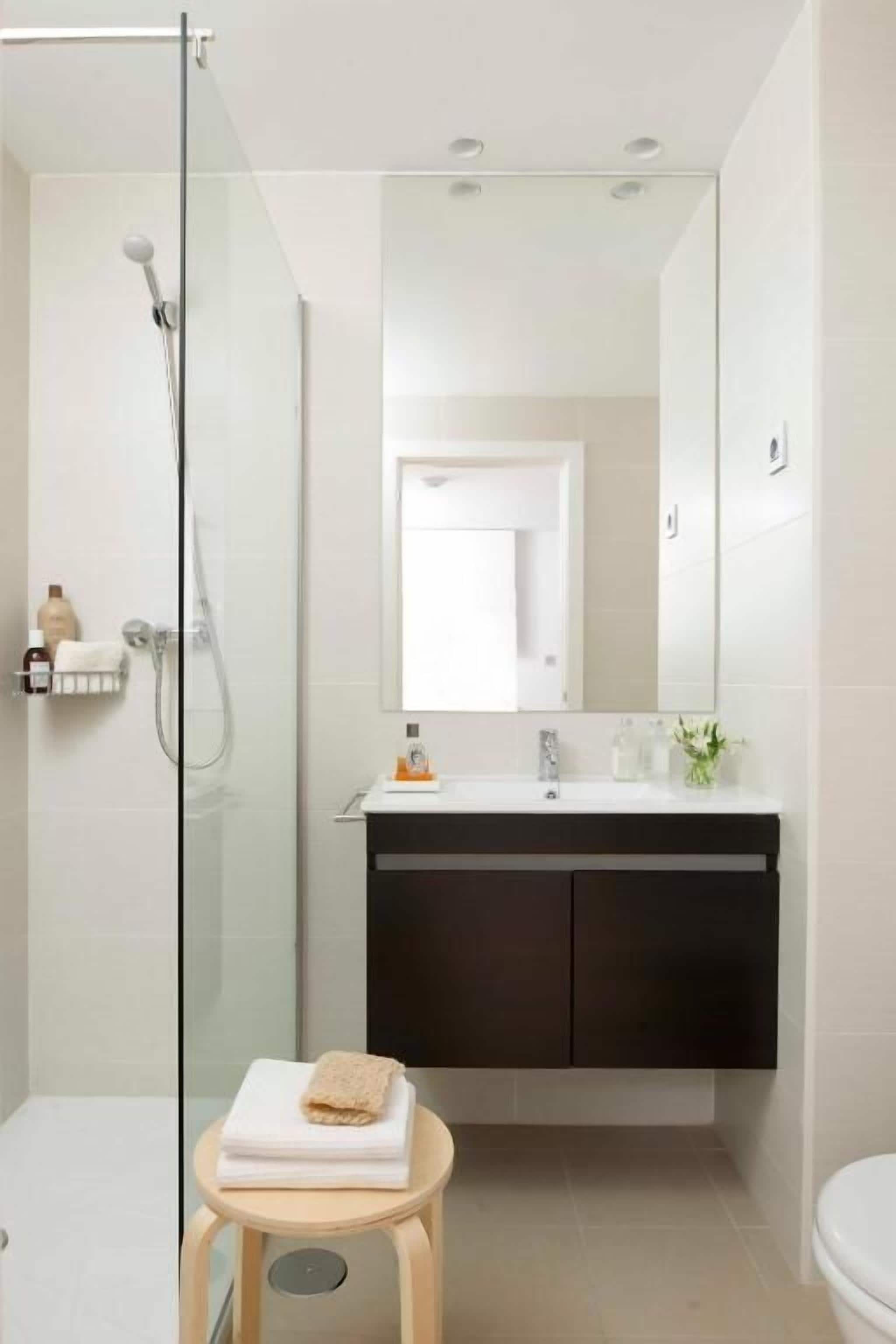 Un baño moderno con ducha envuelta en vidrio, tocador con armarios oscuros y un inodoro.