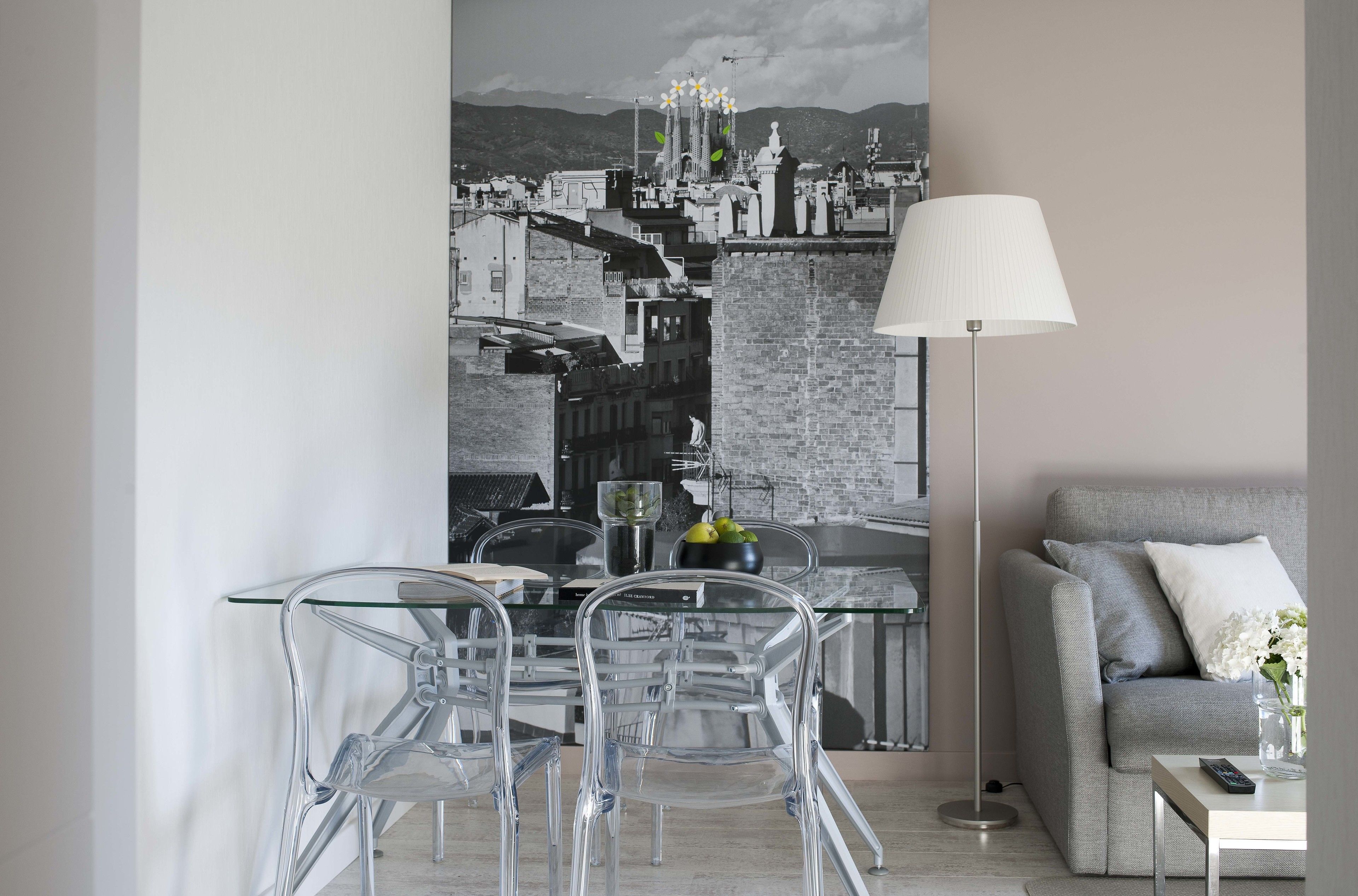 A modern living room with a grey sofa, a glass dining table with clear chairs, and a cityscape painting on the wall.