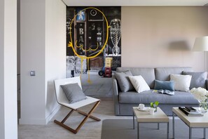 Un salon moderne avec un canapé gris, un fauteuil blanc et une table basse. On y trouve une bibliothèque remplie de livres et d’objets décoratifs.