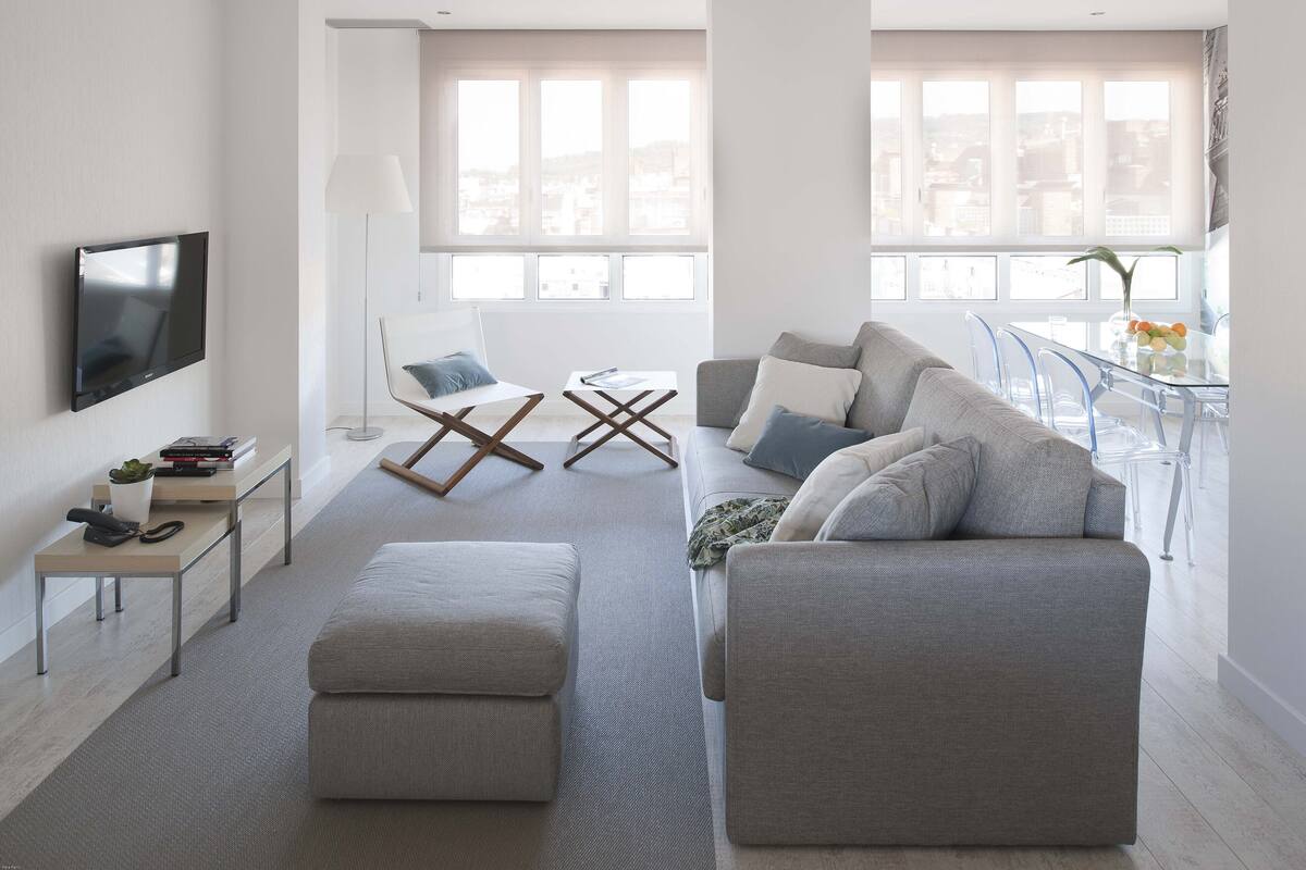 Una sala de estar moderna con un sofá gris, una mesa de centro y un televisor montado en la pared.