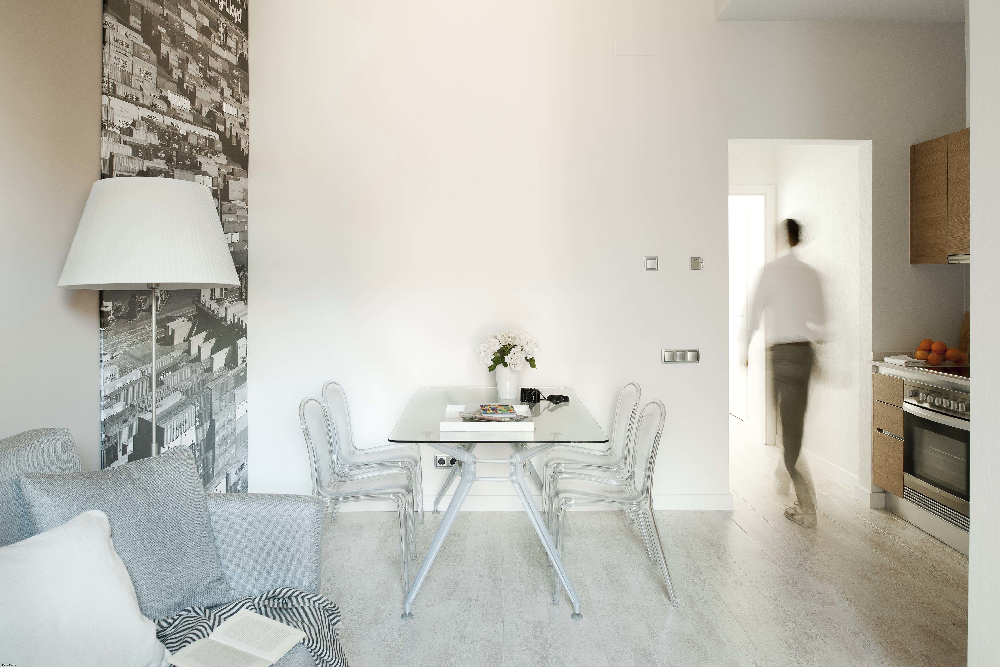 A modern living space with a glass dining table, clear chairs, a grey sofa, and a patterned wall.