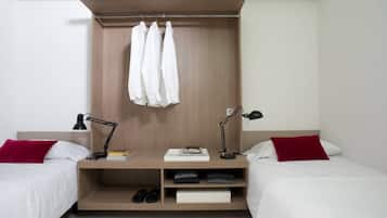Un dormitorio con dos camas, un armario de madera, un escritorio con lámpara y un estante con zapatos.