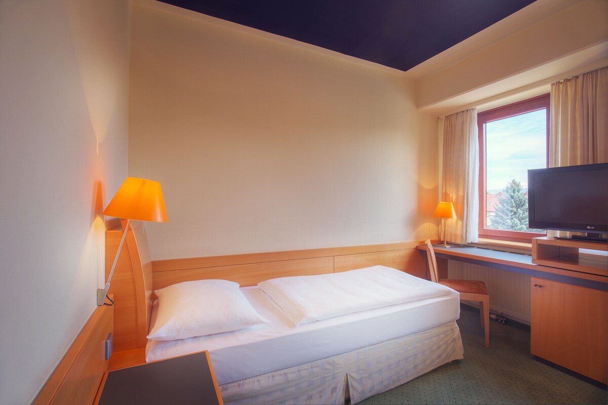 A hotel room with a bed, desk, TV, and lamps.