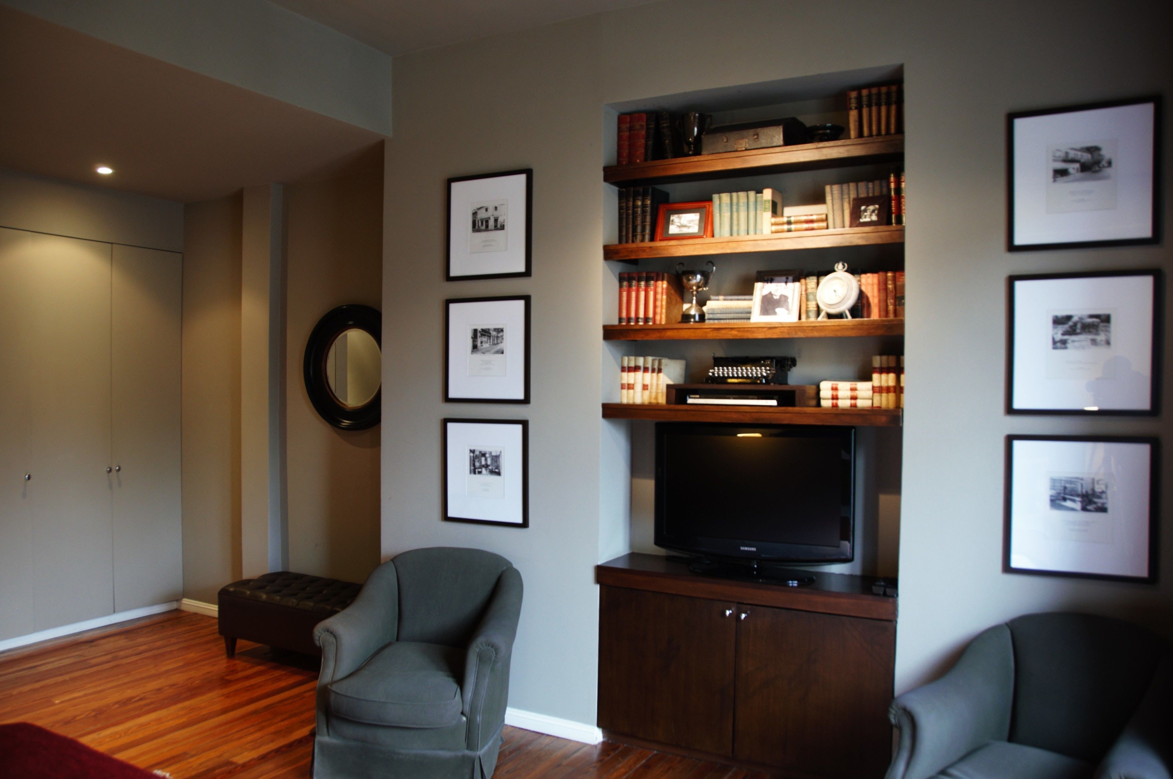 Una sala de estar con televisor, estanterías, cuadros enmarcados y un sillón gris.