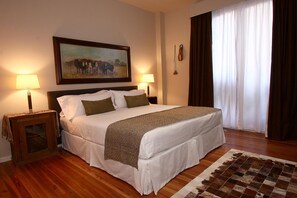 A neatly made bed with a white and brown bedspread, two bedside lamps, a framed painting above the bed, and a window with curtains. - Legado Mitico Buenos Aires (Buenos Aires)
