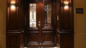 Una puerta doble de madera con una lámpara encima, que da a un pasillo alfombrado.