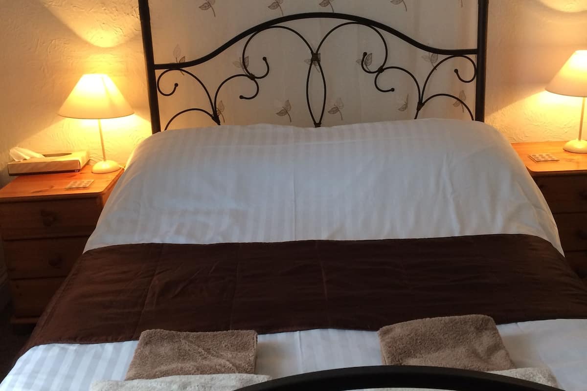A four-poster bed with a white and brown bedspread, two bedside lamps, and a butterfly-patterned curtain.