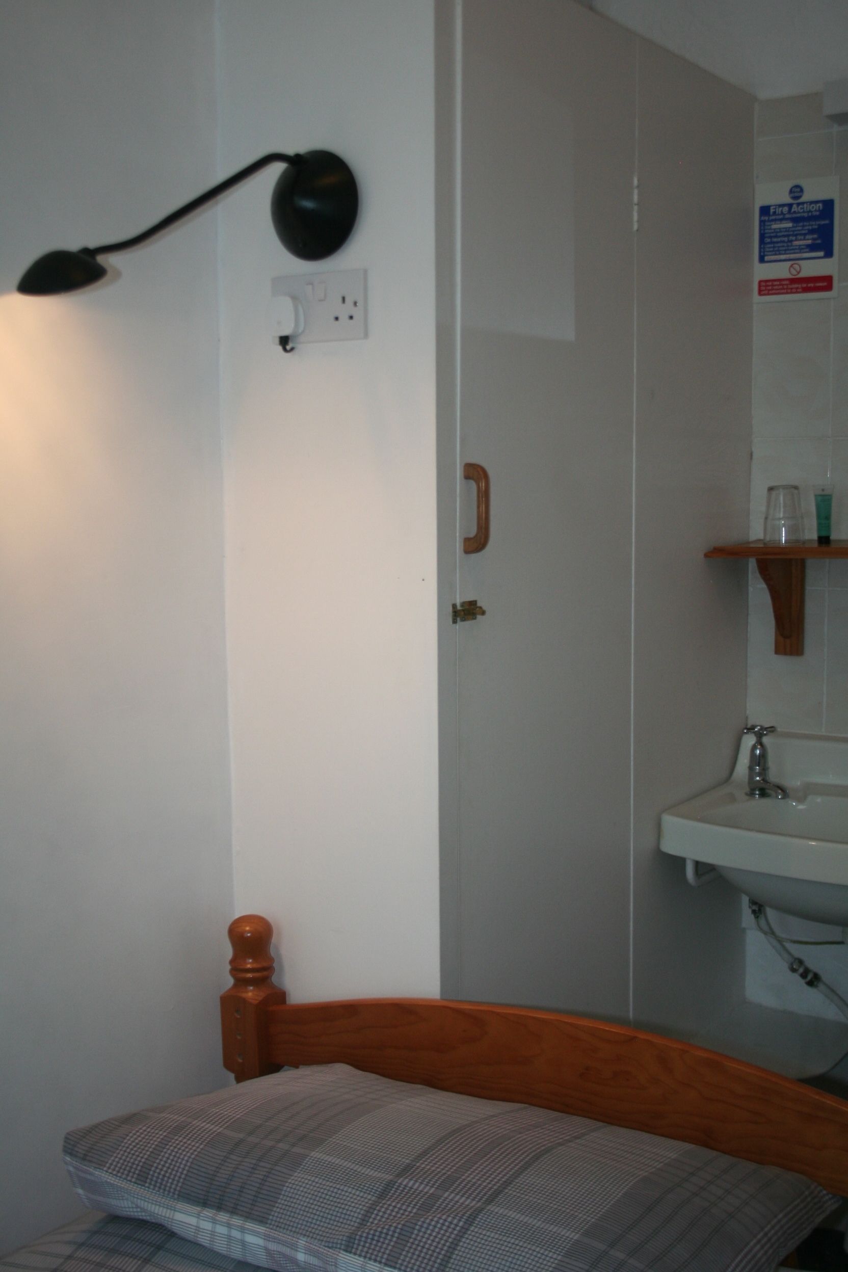 A bedroom with a wooden headboard, a bedside table, a lamp, a mirror, and a shelf with toiletries.