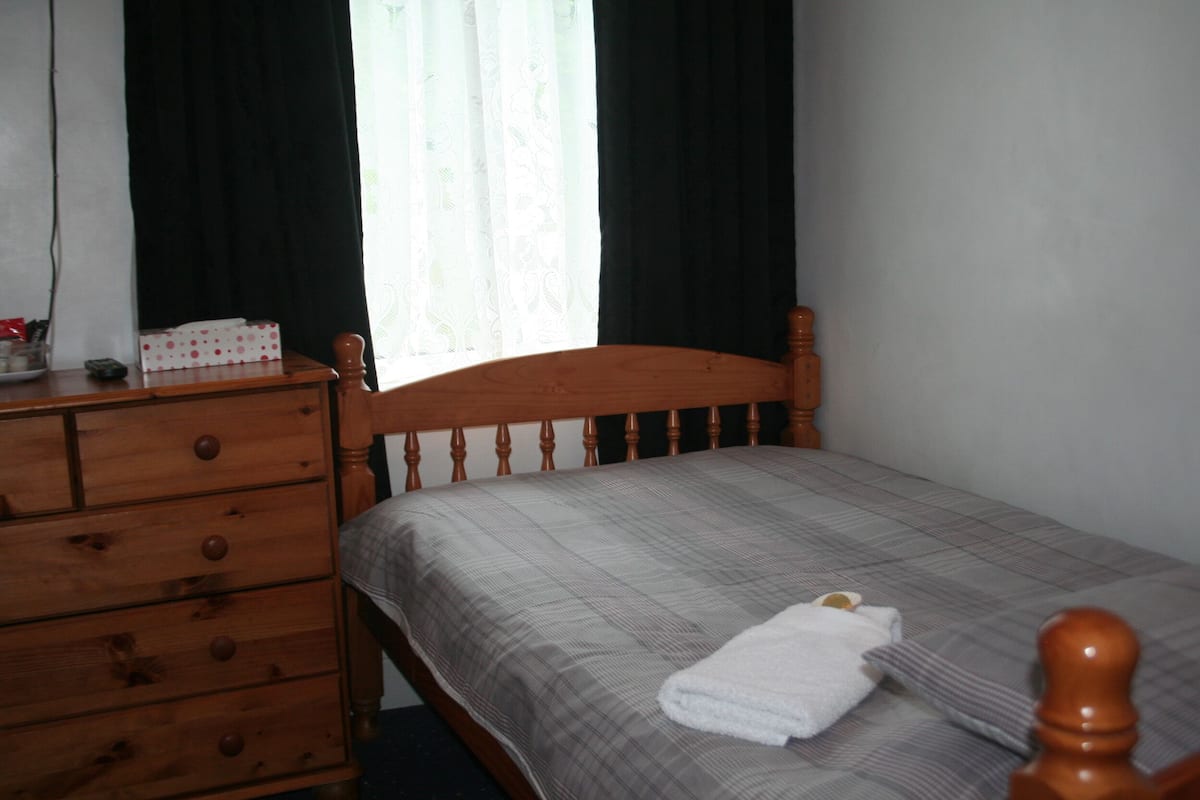 A bedroom with a wooden bed frame, a dresser with drawers, and a window with curtains.