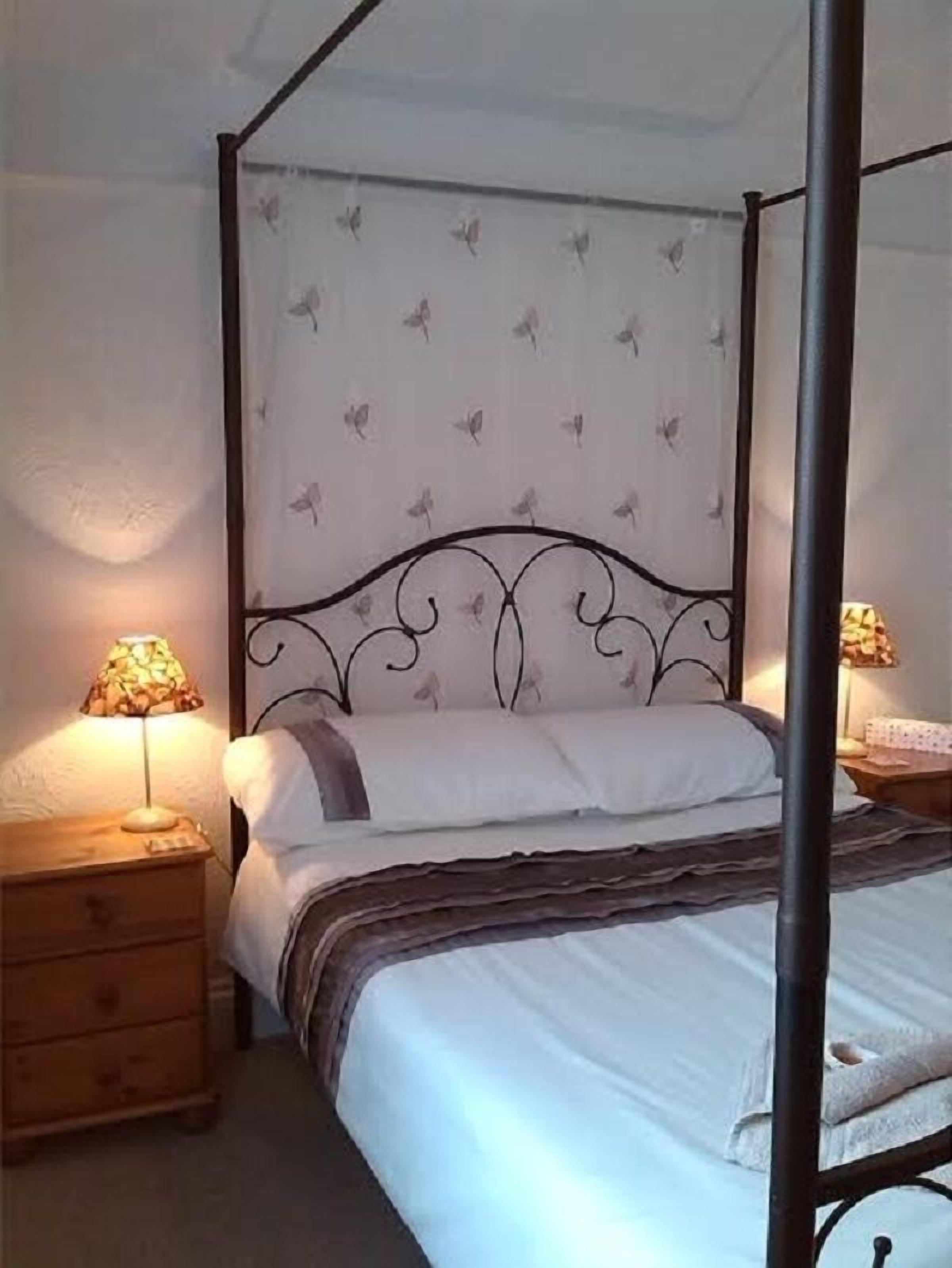 A four-poster bed with a white canopy and butterfly pattern, flanked by wooden nightstands with lamps.