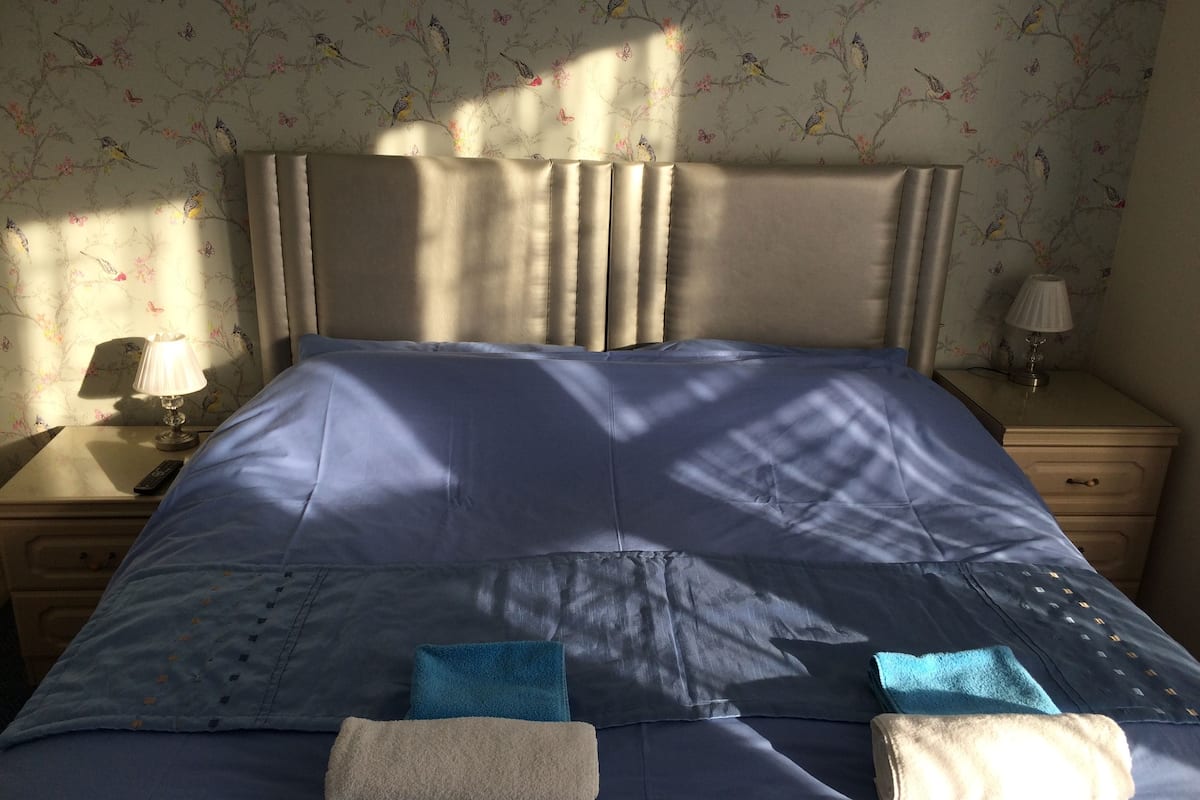 A neatly made bed with a blue bedspread, two towels, and a nightstand with a lamp.