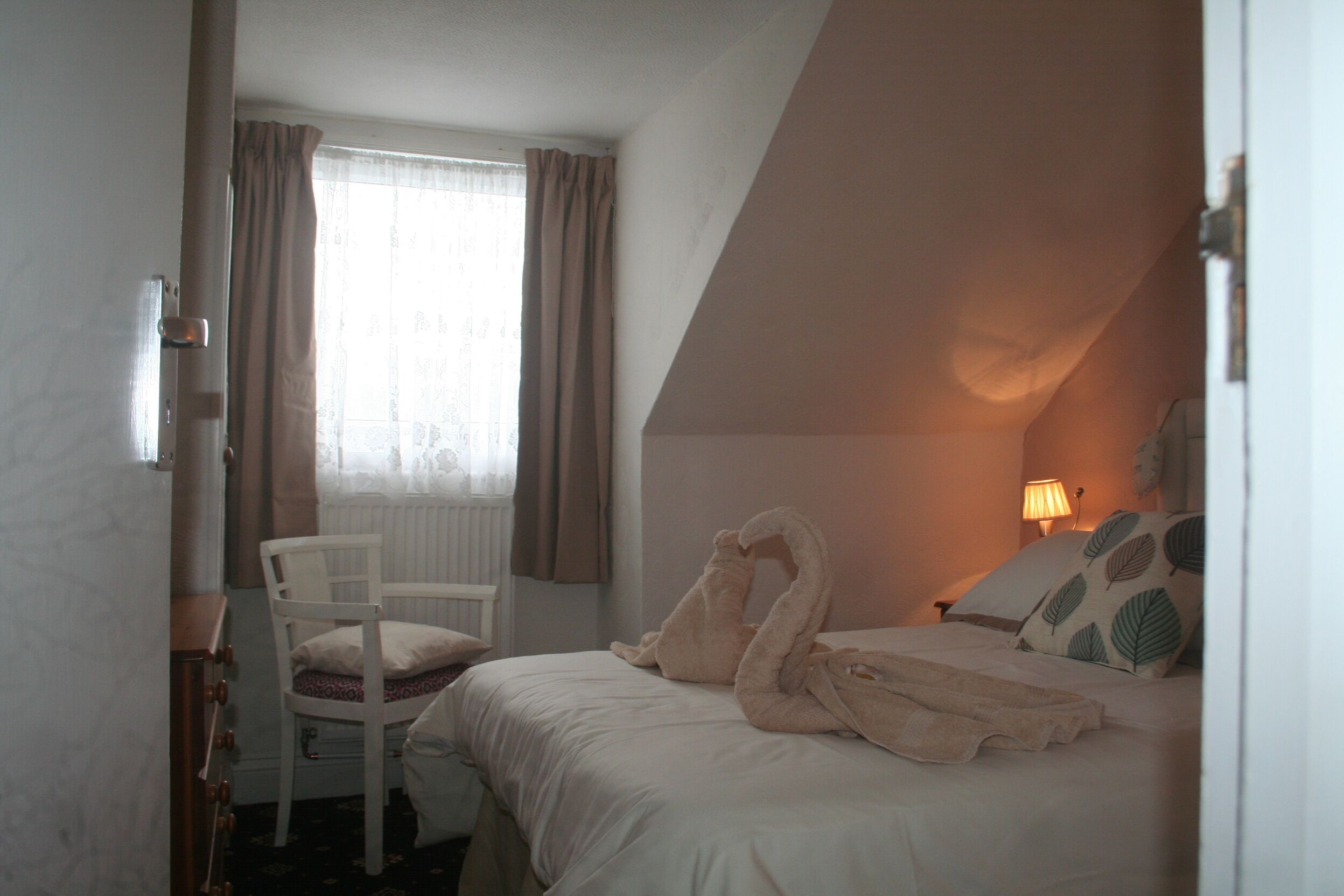 Une chambre à coucher avec un lit, une chaise, une fenêtre avec des rideaux et une lampe.
