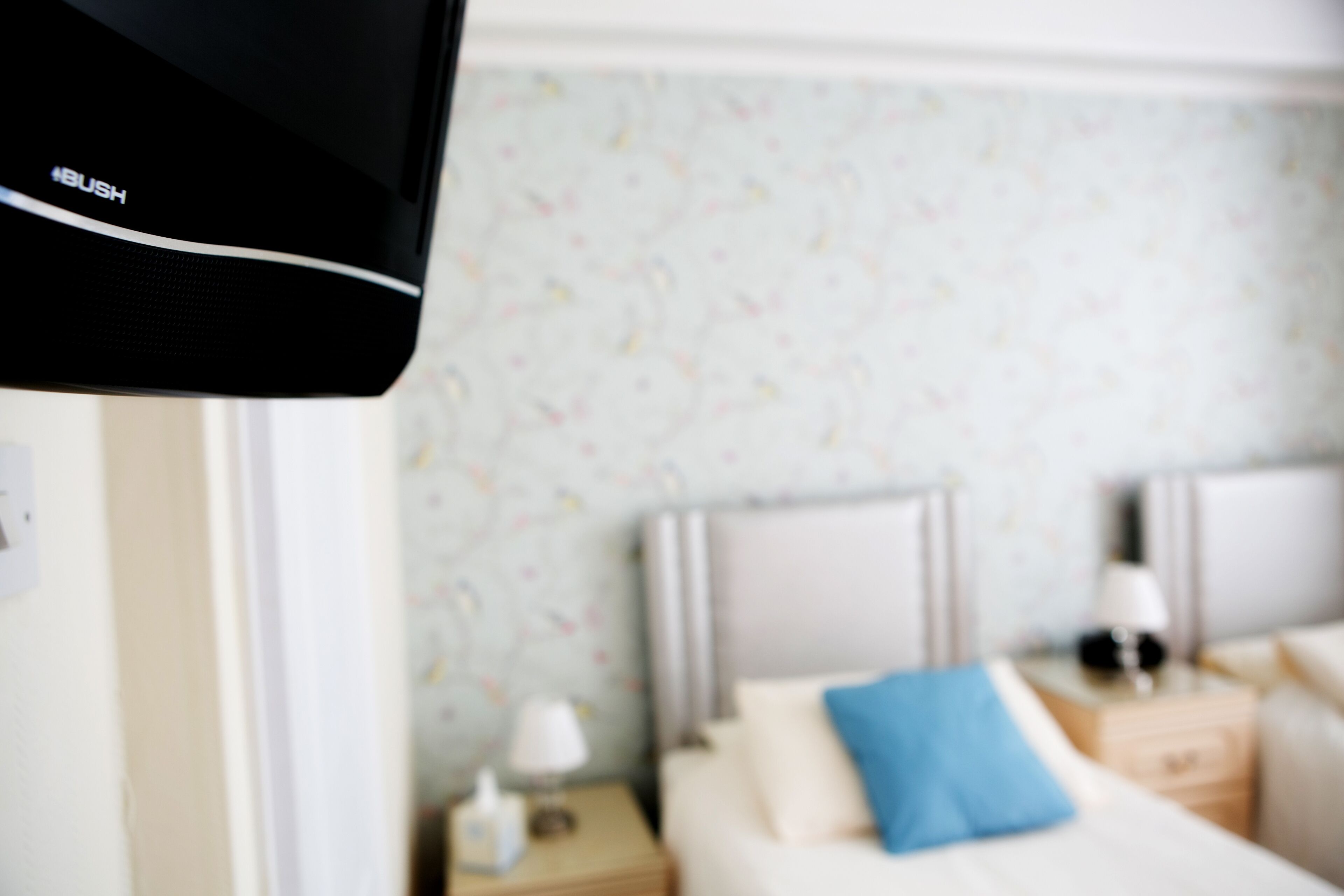 A hotel room with a bed, a nightstand, a lamp, and a wall with a floral pattern.