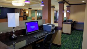 A hotel reception area with a computer, desk, chairs, and a lamp. - Fairfield Inn & Suites Flint Fenton (Fenton)