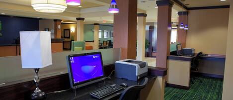 A hotel reception area with a computer, desk, chairs, and a lamp.