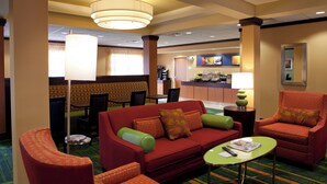 A hotel lobby with a red sofa, green armchairs, a coffee table, and a large chandelier. - Fairfield Inn & Suites Flint Fenton (Fenton)