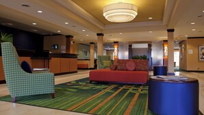 A lobby with a green patterned armchair, a red sofa, and a blue ottoman. - Fairfield Inn & Suites Flint Fenton (Fenton)