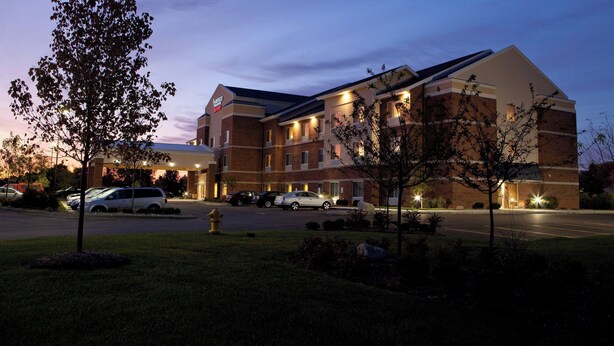 A hotel with a brick facade, multiple windows, and a parking lot with several cars. - Fairfield Inn & Suites Flint Fenton (Fenton)