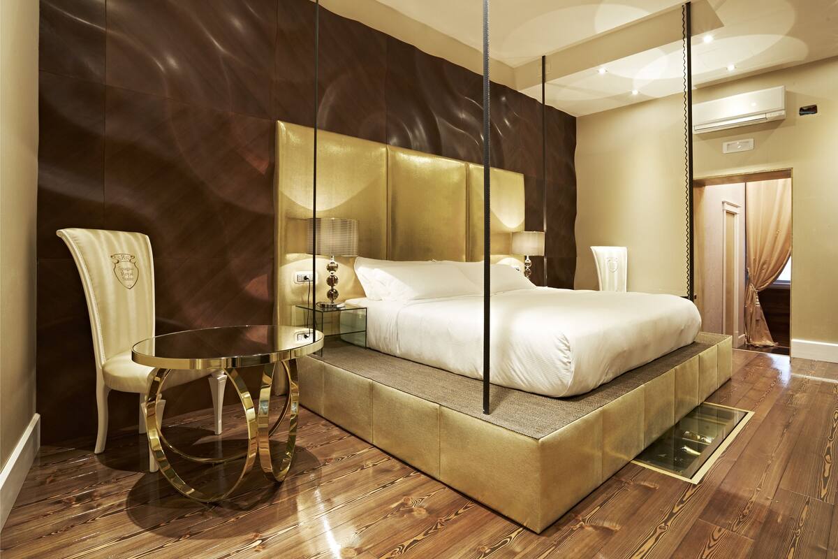 Una habitación de hotel moderna con una cama grande, una mesita de vidrio, una silla y un televisor integrado.
