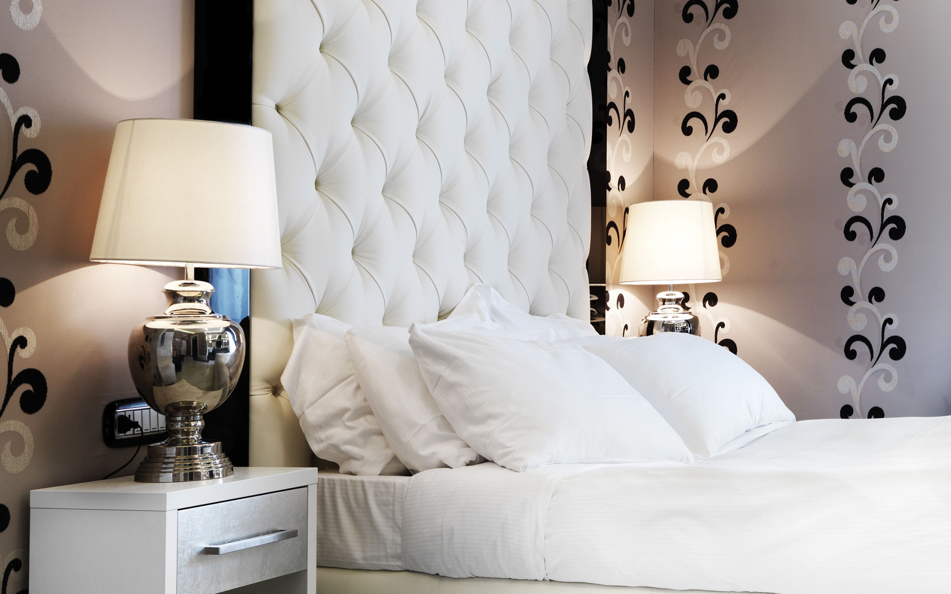 A neatly made bed with white linens, a tufted headboard, and two bedside lamps.