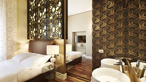 Une chambre d’hôtel comprenant un lit, des tables de chevet, un miroir, un mur orné d’un motif géométrique, une télévision et une salle de bain avec un lavabo et un miroir.