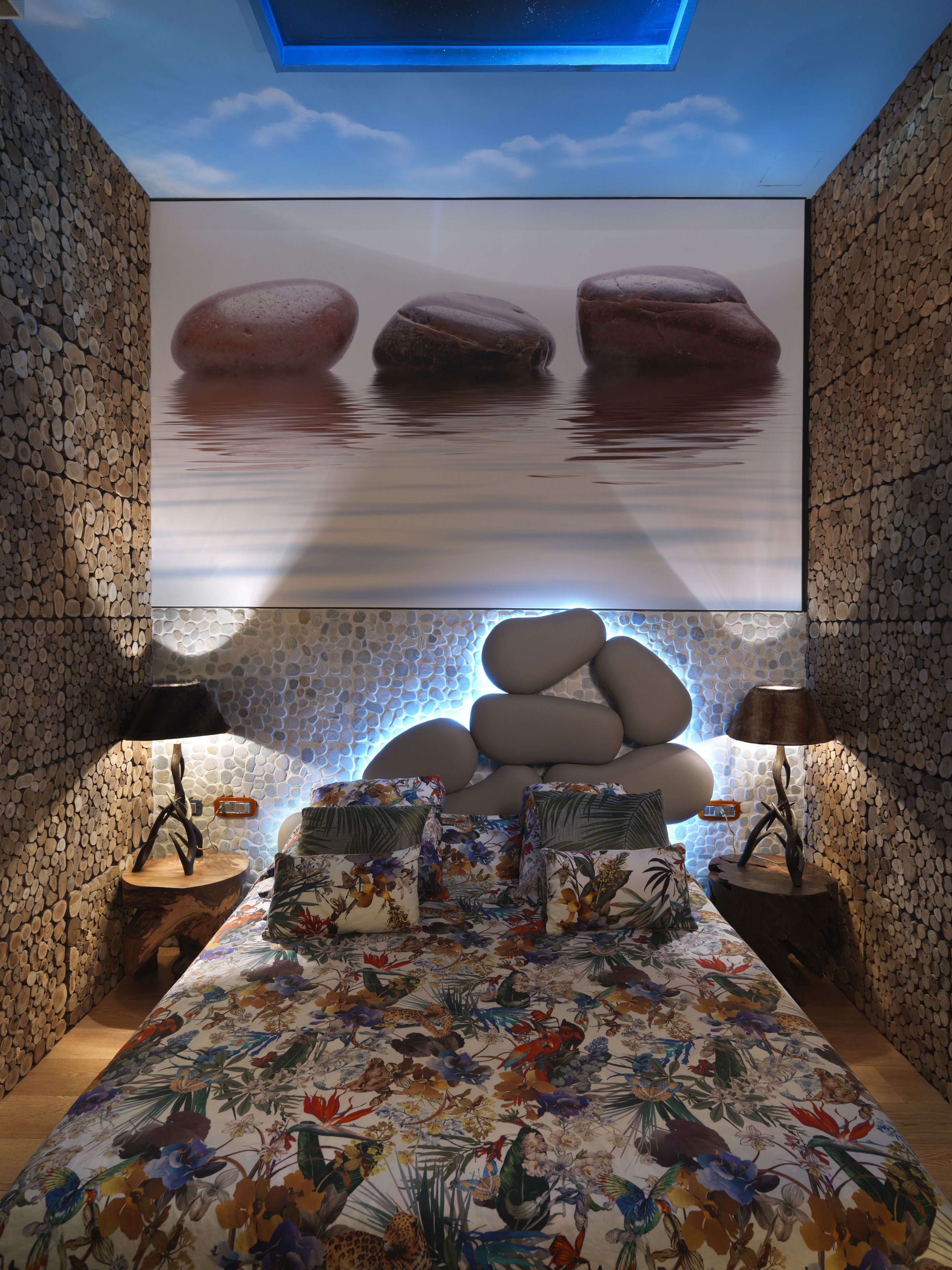Una habitación con una cama, una pared decorada con rocas y un techo que simula un cielo estrellado.