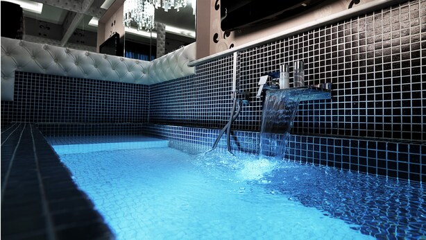 Une piscine à l’eau d’un bleu limpide, avec des murs carrelés et un élément décoratif aquatique.