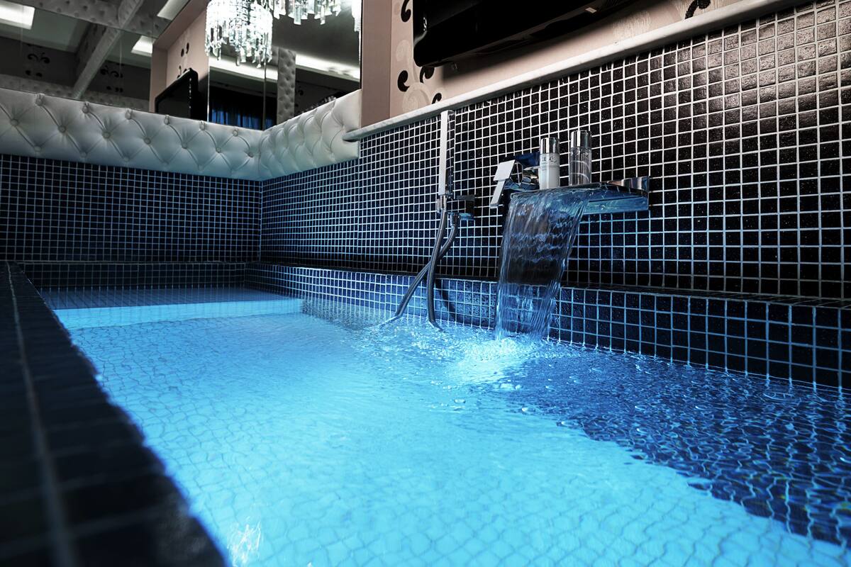 Una piscina con agua azul cristalina, paredes con azulejos y una fuente.