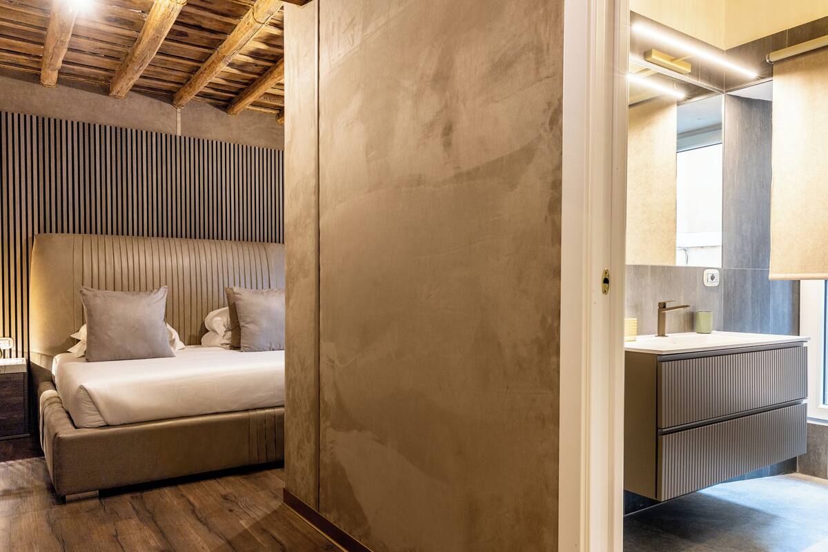 Un dormitorio moderno con una cama grande, techo de madera y baño con espejo y lavamanos.