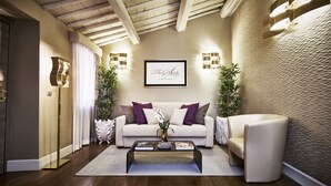 Un salon avec un canapé, un fauteuil et une table basse. Un tableau encadré est accroché au mur, et deux lampes sont fixées au mur.