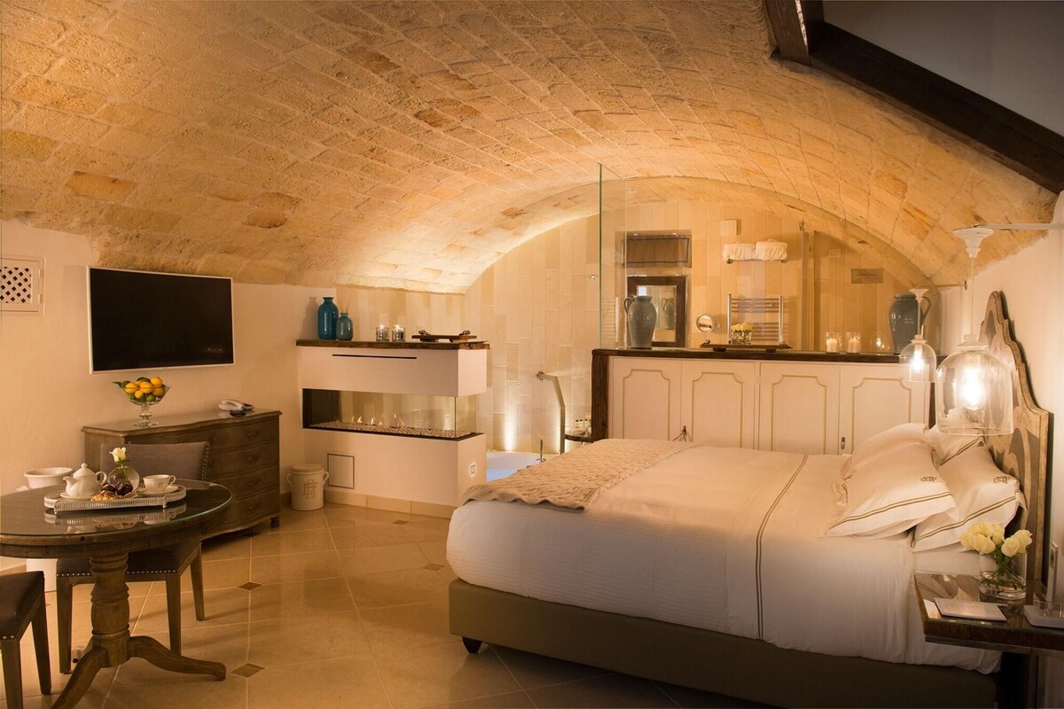 A cozy bedroom with a large bed, a dining table, and a kitchen area with a modern design.