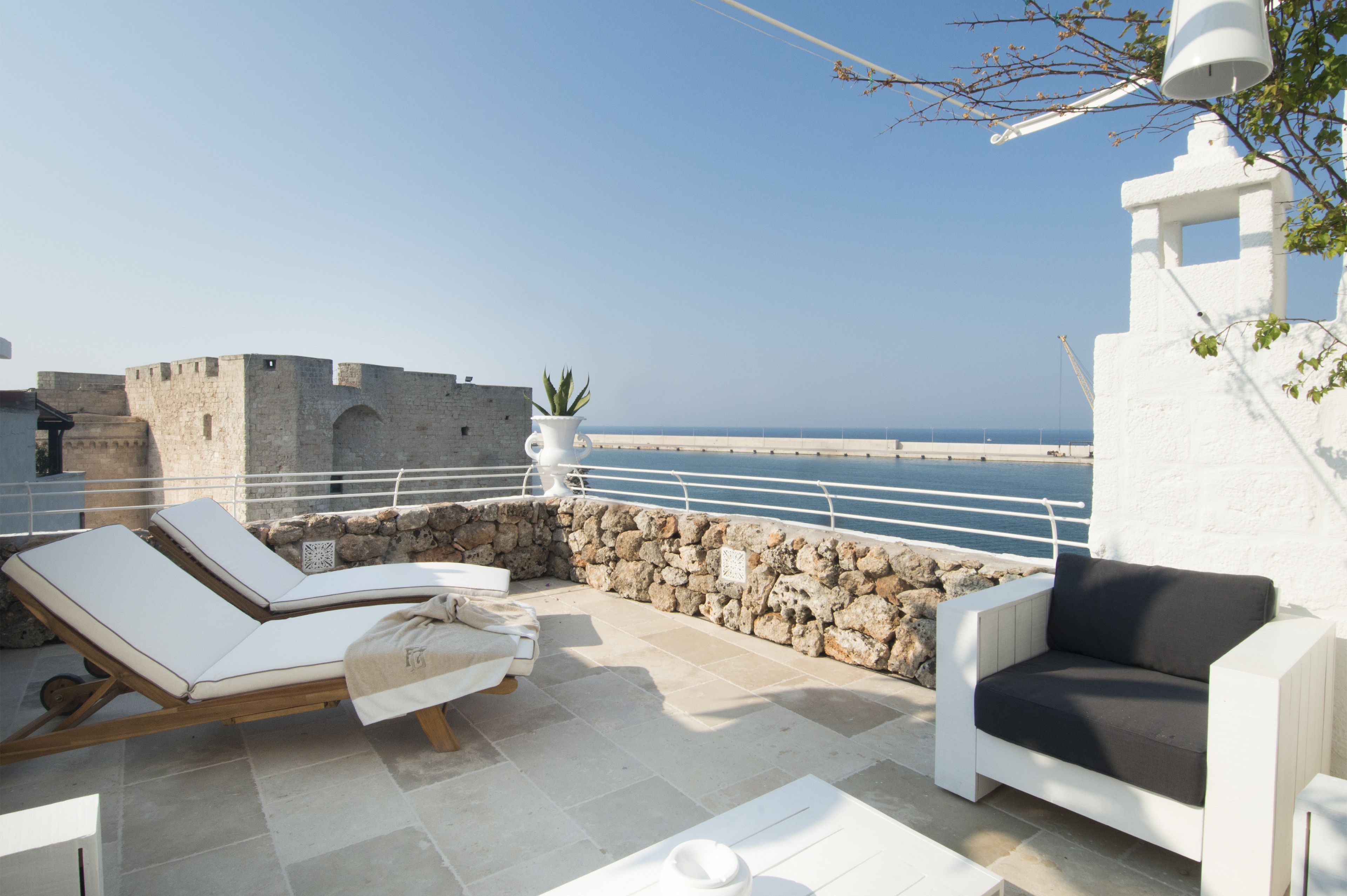 A terrace with two lounge chairs, a potted plant, and a view of the sea.