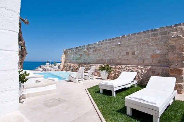 A pool area with lounge chairs and a stone wall, overlooking the sea. - Don Ferrante - Dimore di Charme (Monopoli)