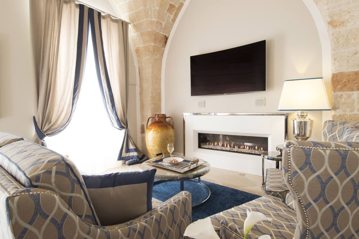 A living room with a fireplace, a television mounted on the wall, and a large vase on the coffee table.