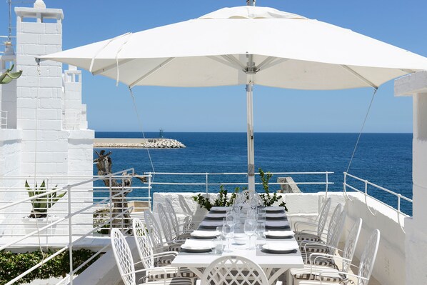 A table set for dining with a white umbrella, white chairs, and a view of the sea. - Don Ferrante - Dimore di Charme (Monopoli)