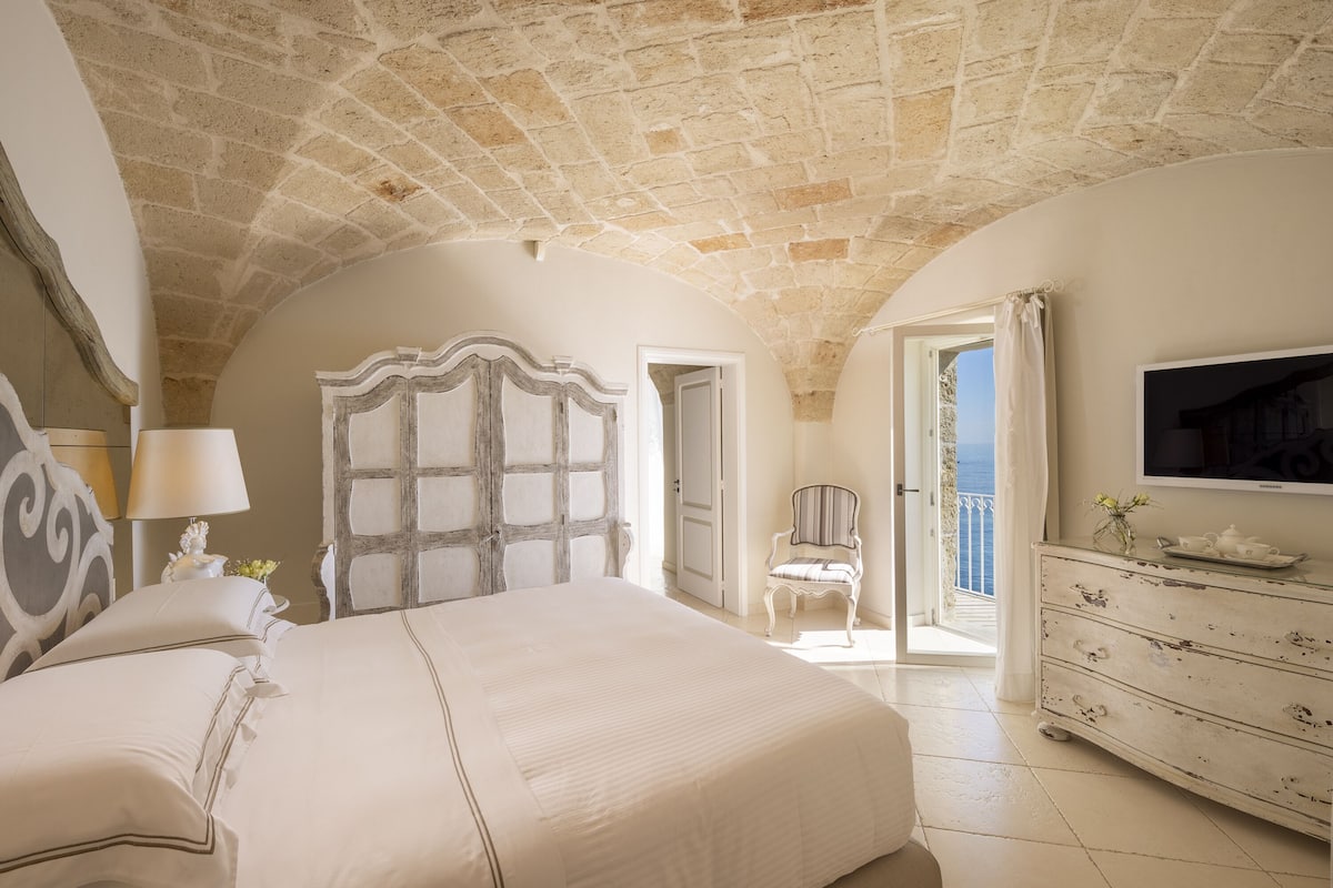 A bedroom with a stone ceiling, a bed, a chair, a dresser, and a television.