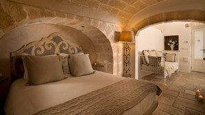 A bedroom with a stone wall, a bed with a headboard, a bedside lamp, and a small table with a vase.
