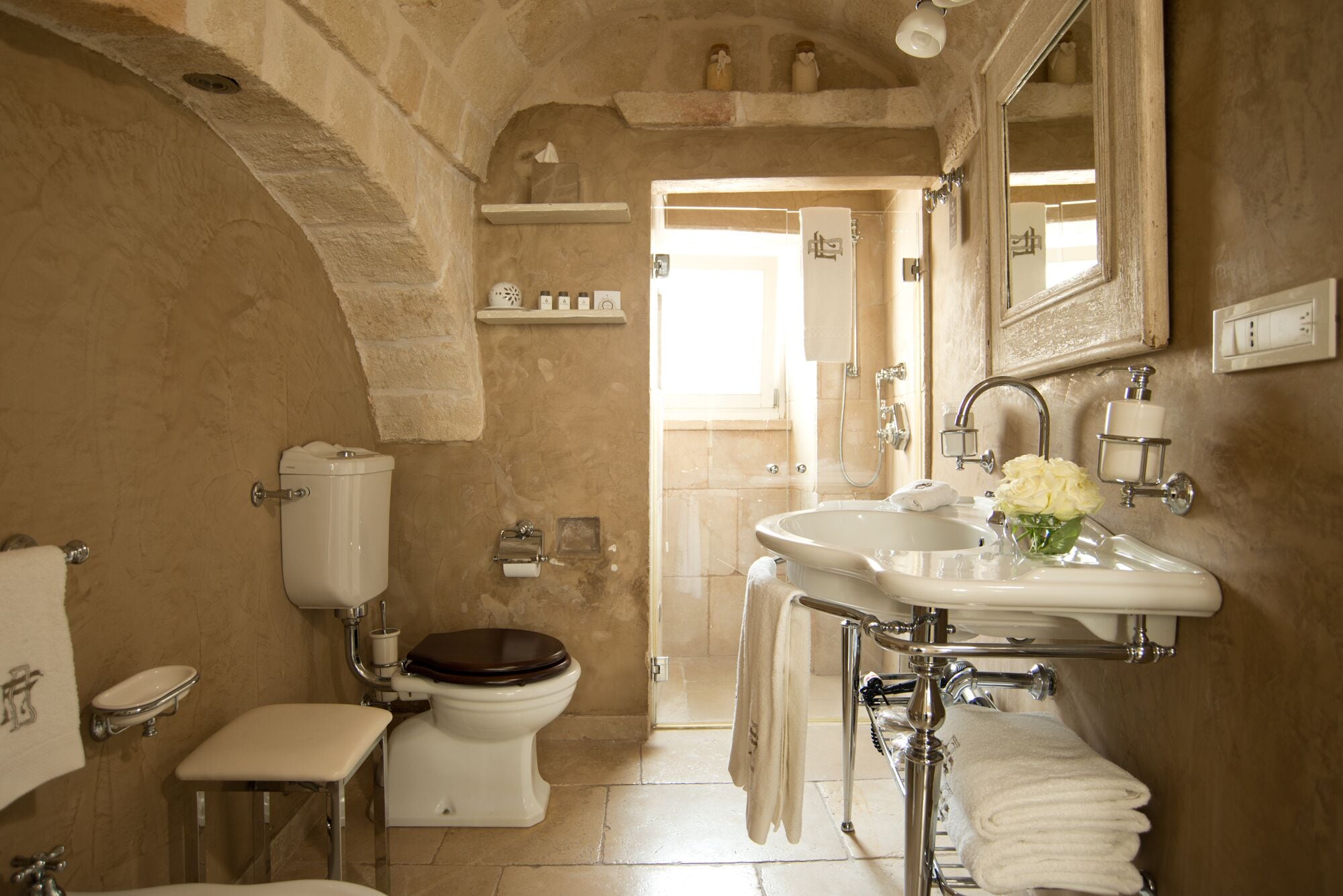 Un bagno con il water, un lavandino e una doccia. È presente un portasciugamani e uno specchio sopra il lavandino.
